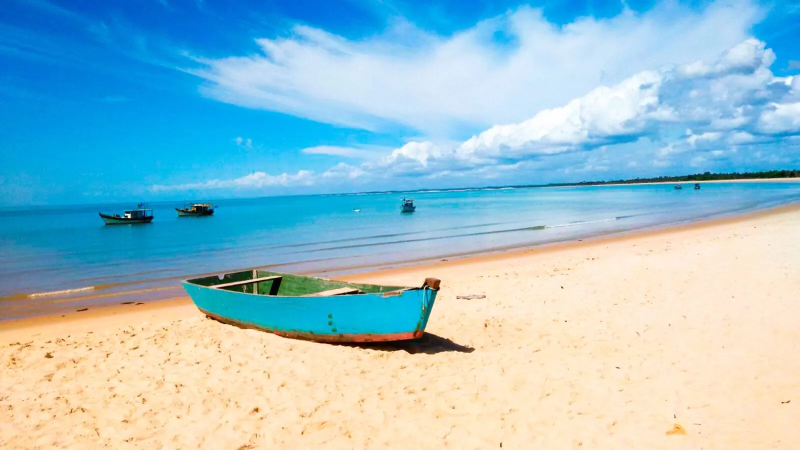 Barco de pesca azul sobre a areia da praia de Corumbau, com pequenas embarcações no mar